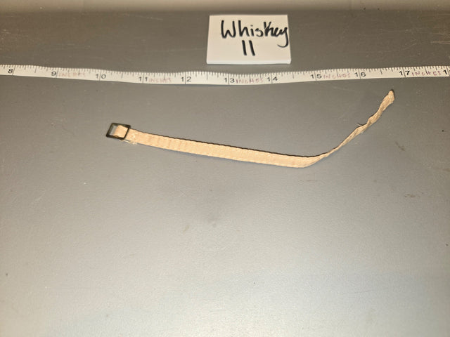 Looking at the item, it appears to be a watch strap/band with a small buckle hardware, measuring approximately 7-8 inches long against the ruler, consistent with 1/6 scale. The tag reads "Whiskey II". 1/6 Scale WWII US Watch Strap - Whiskey II
